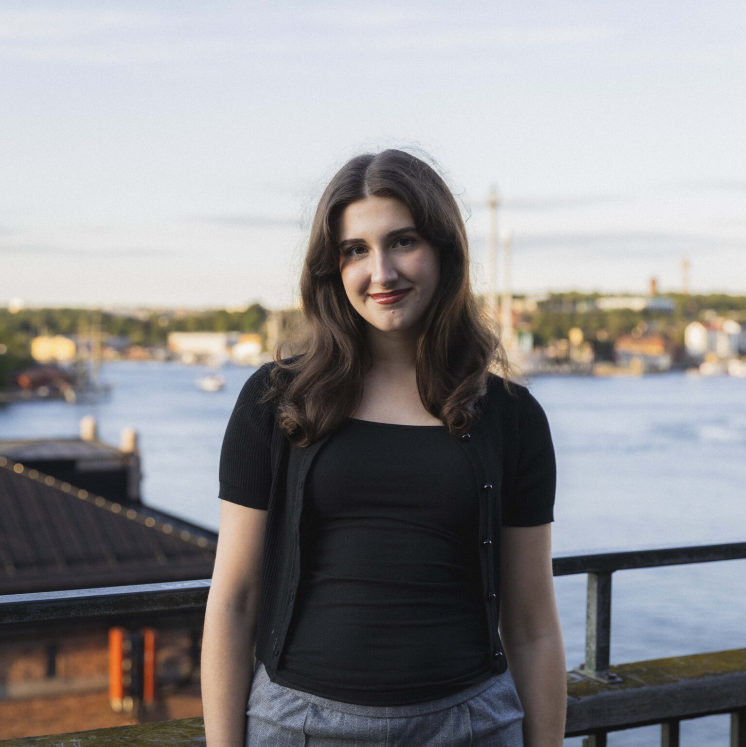 Headshot of Katie Whelan on a balcony overlooking the Stockholm skyline, wearing a black cardigan