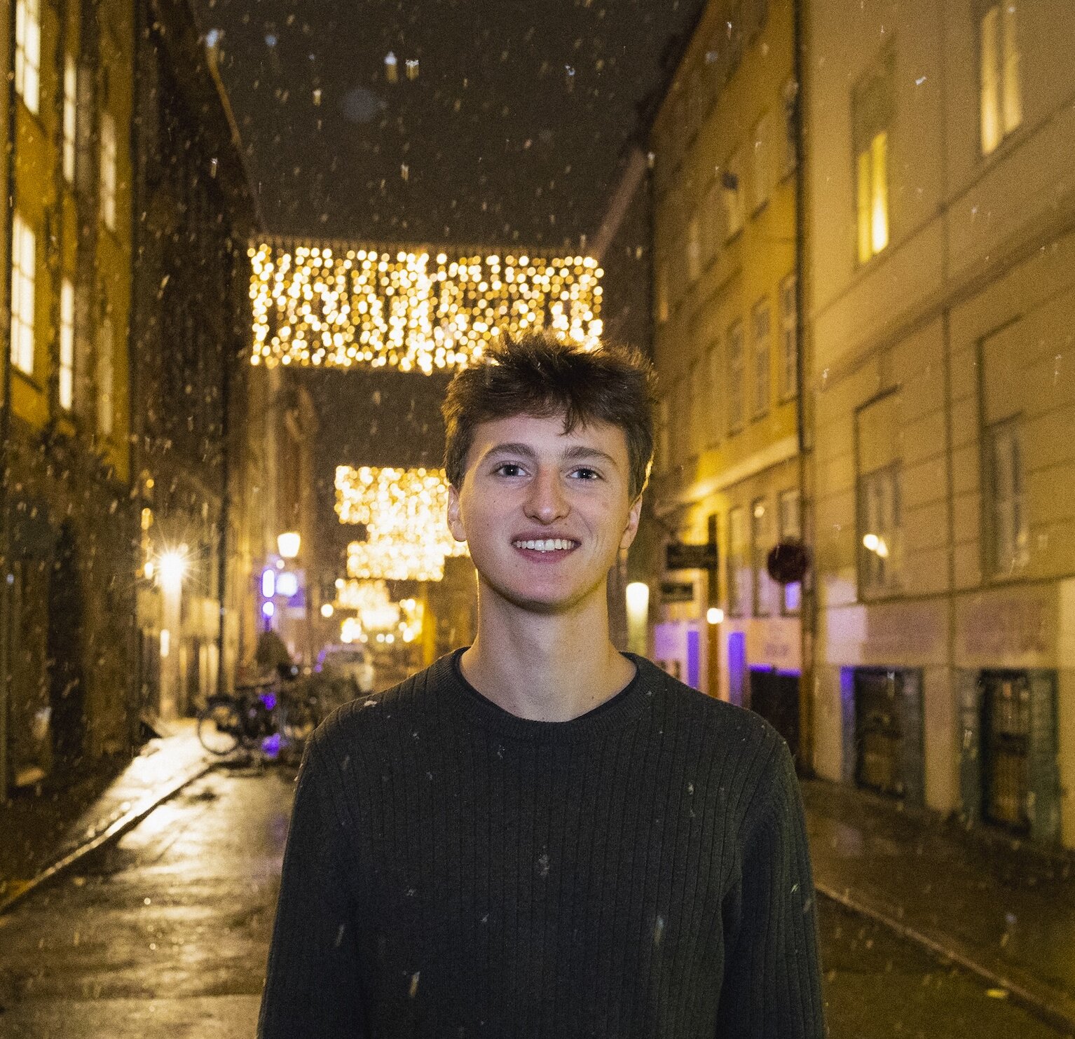 Night time headshot of Brady Prosser on a Copenhagen street in the snow, wearing a black sweater