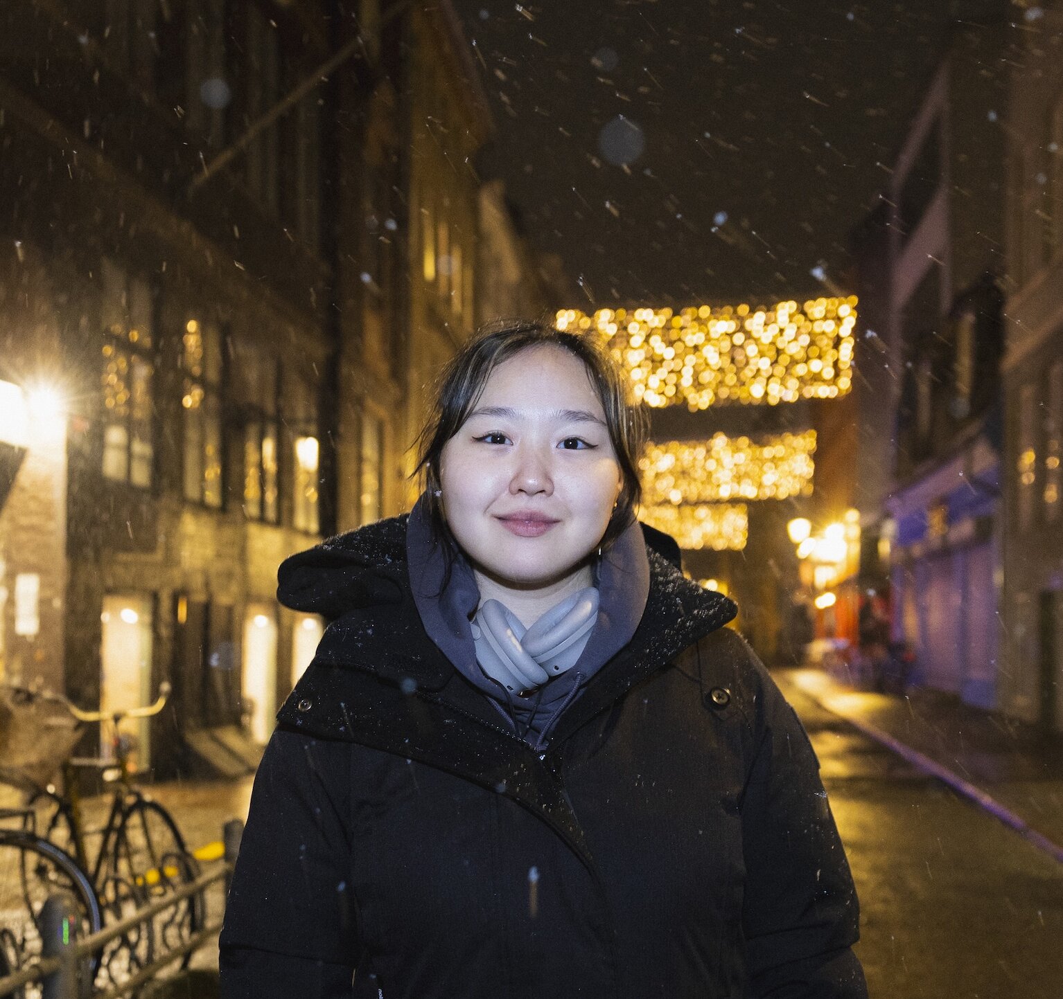 Night time headshot of Chae Rin Choi on a Copenhagen street in the snow, wearing a black puffer jacket