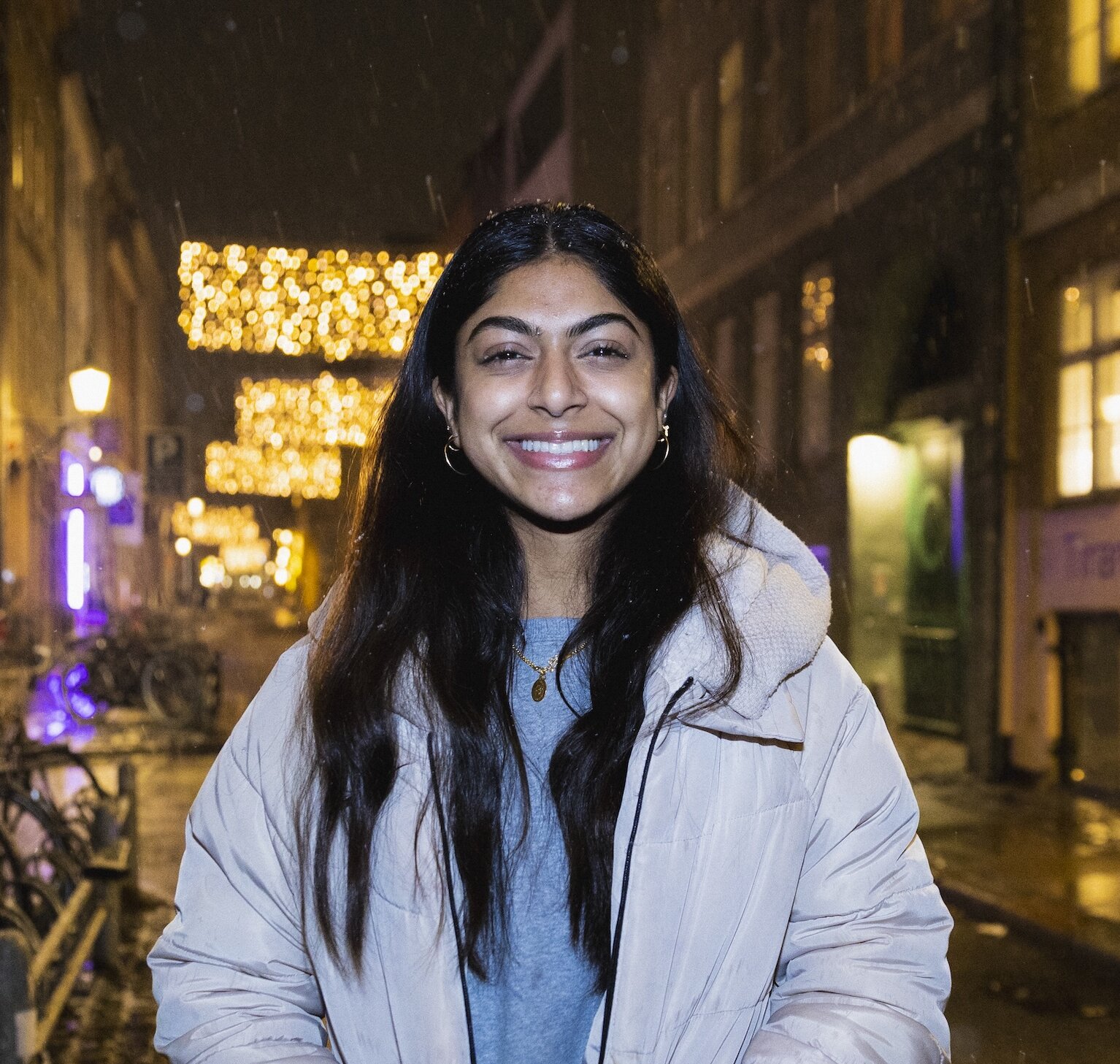Night time headshot of Janaki Nair on a Copenhagen street in the snow, wearing a beige puffer jacket