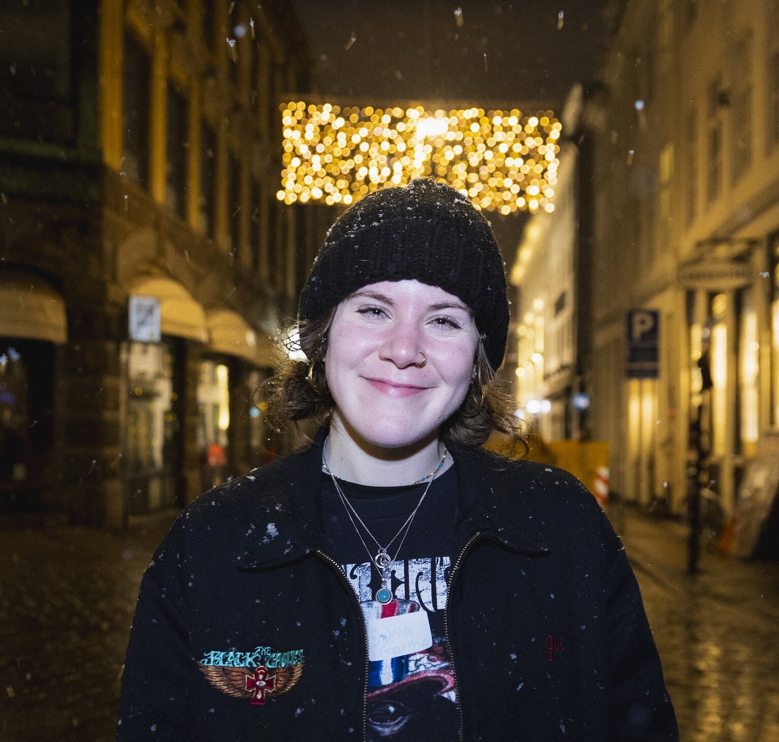 Night time headshot of Sophia Garthe on a Copenhagen street in the snow, wearing a beanie and a black jacket