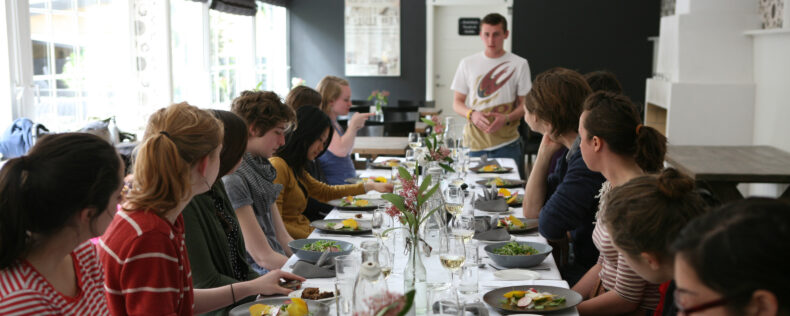 Students being told about their food at a long table.
