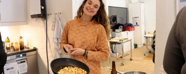 A student smiling with a pan of food that she is prepping..