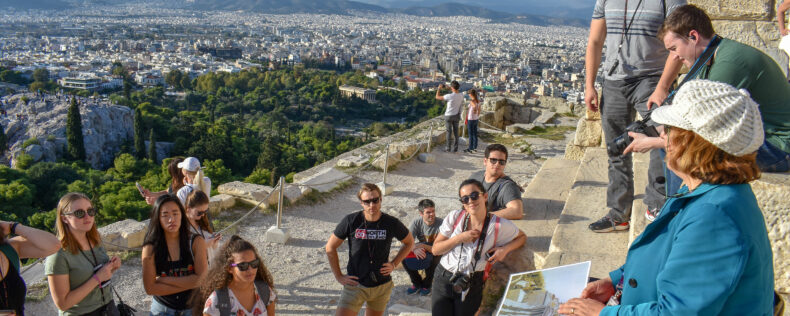 Students receiving a lecture from a vista point looking over a Greek city.