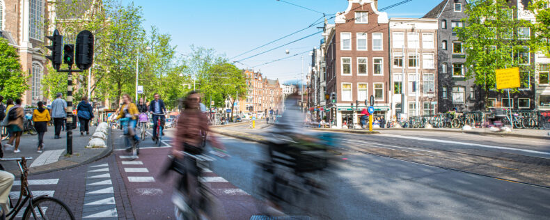 Long exposure image of people biking through Amsterdam streets during a sunny day.