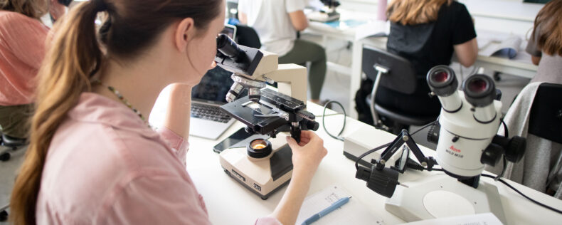 A student examining materials under a microscope during lab class.