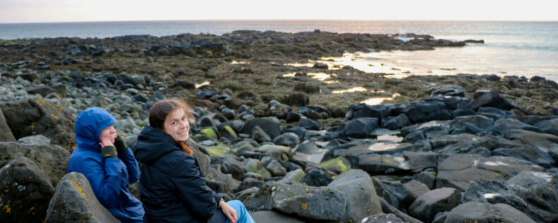 Students sitting on rocks near the Icelandic sea. Looking back and smiling at the camera.