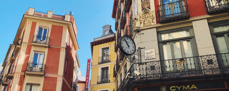 Walking through the intimate streets of Madrid. The buildings are shades of orange and yellow and it's a sunny day.
