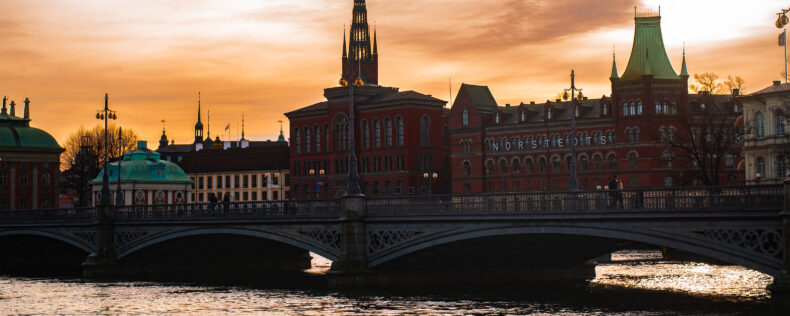 Golden hour over Stockholm. Historic Swedish buildings in the background, an arch bridge, and water in the foreground.