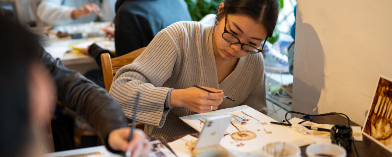 A student painting flower with brown acrylic ink during a class session.