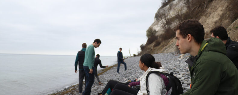 Students sitting on the rocks of Møns Klint, looking out into the water. The day is overcast and it is late Autumn.