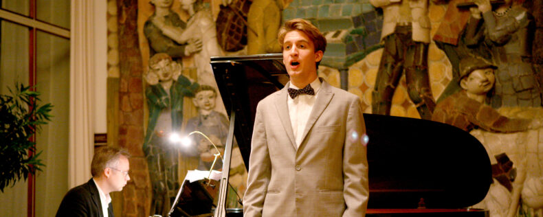 Young man in formal attire singing with a piano player.