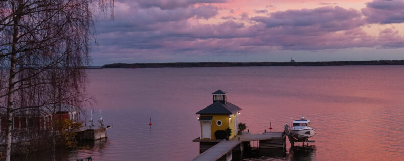 Over looking a Swedish lake during golden hour. There is a pastel pink sky covering the horizon.